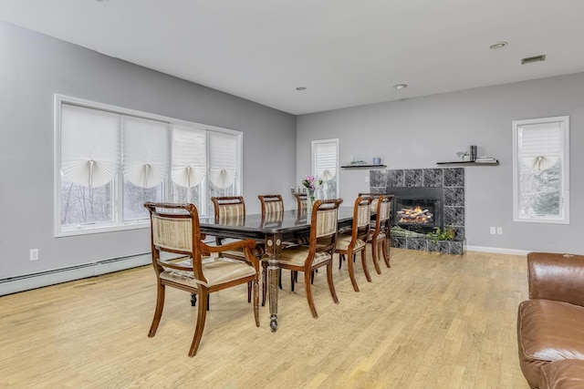 dining space featuring a fireplace, light hardwood / wood-style floors, and a baseboard heating unit