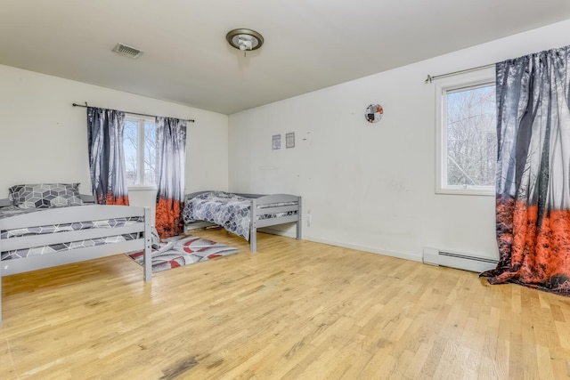 bedroom featuring baseboard heating, multiple windows, and light hardwood / wood-style floors