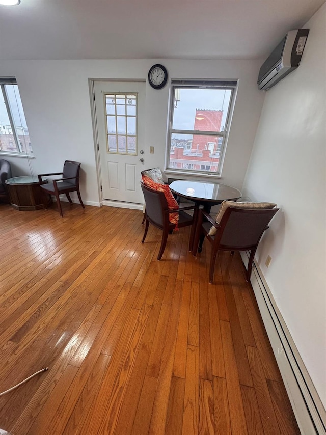 dining space featuring a wall mounted air conditioner, hardwood / wood-style flooring, and a baseboard heating unit