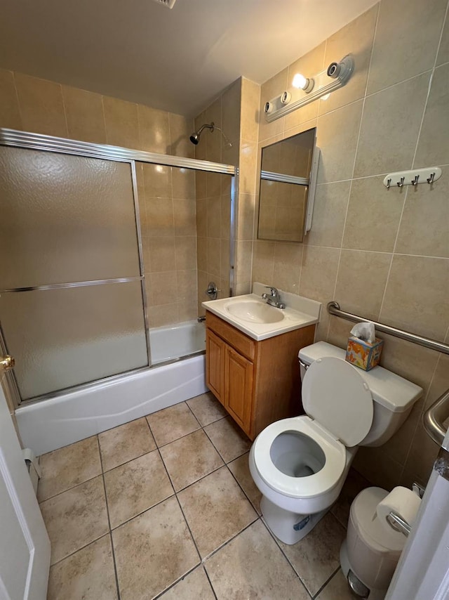 full bathroom featuring vanity, shower / bath combination with glass door, tile patterned flooring, toilet, and tile walls