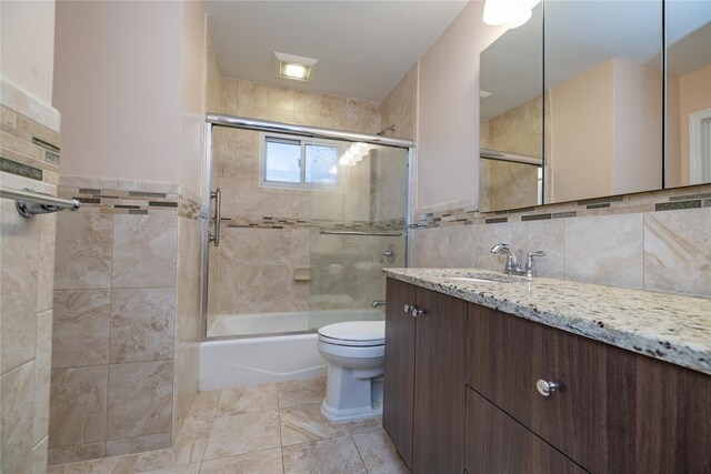 full bathroom featuring shower / bath combination with glass door, vanity, toilet, and tile walls