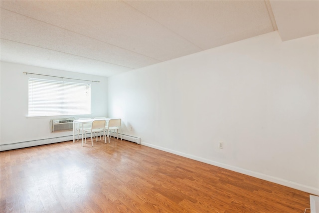 unfurnished room with a wall mounted AC, wood-type flooring, and a baseboard heating unit