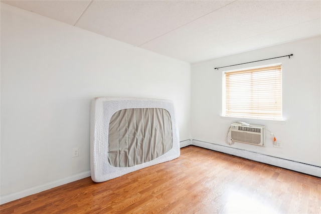 empty room with wood-type flooring, an AC wall unit, and a baseboard radiator