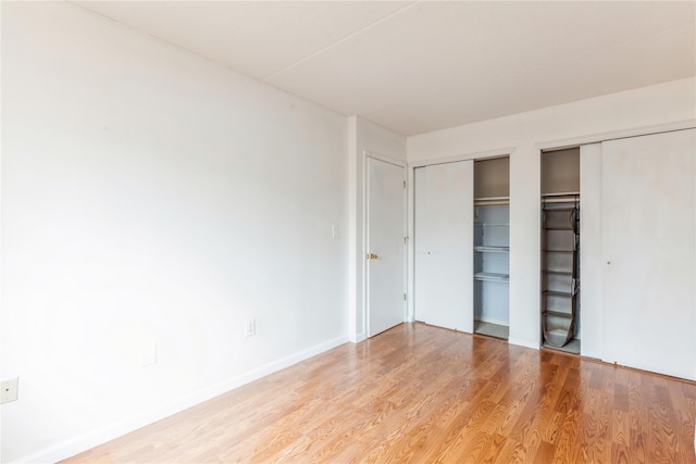 unfurnished bedroom featuring light wood-type flooring and two closets