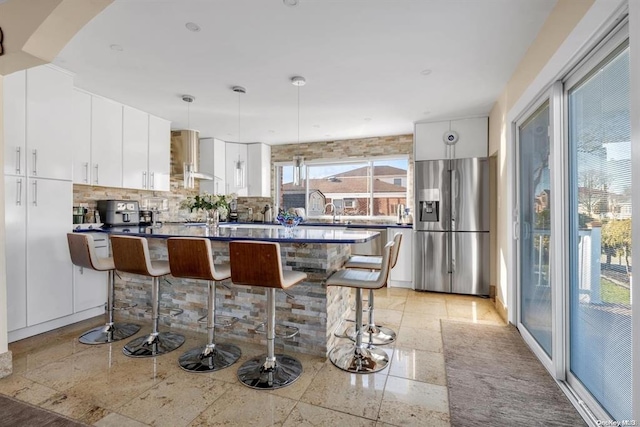 kitchen featuring stainless steel refrigerator with ice dispenser, white cabinetry, hanging light fixtures, and a breakfast bar area