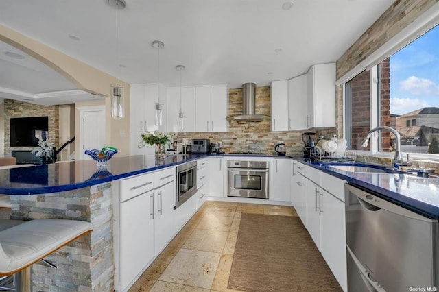 kitchen with decorative light fixtures, white cabinetry, wall chimney range hood, and stainless steel appliances