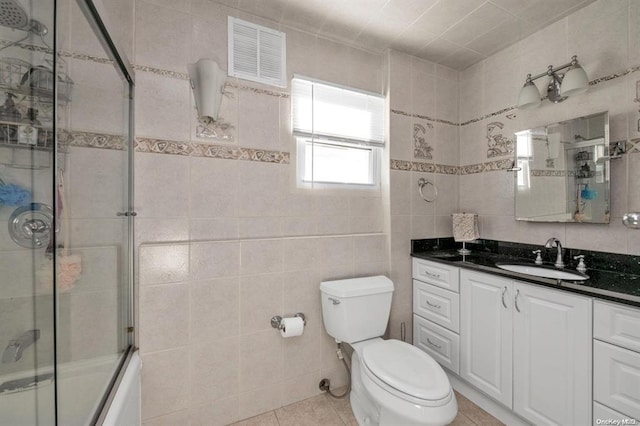 full bathroom featuring tile patterned floors, toilet, shower / bath combination with glass door, vanity, and tile walls