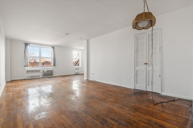 unfurnished living room featuring hardwood / wood-style flooring, radiator heating unit, and an AC wall unit