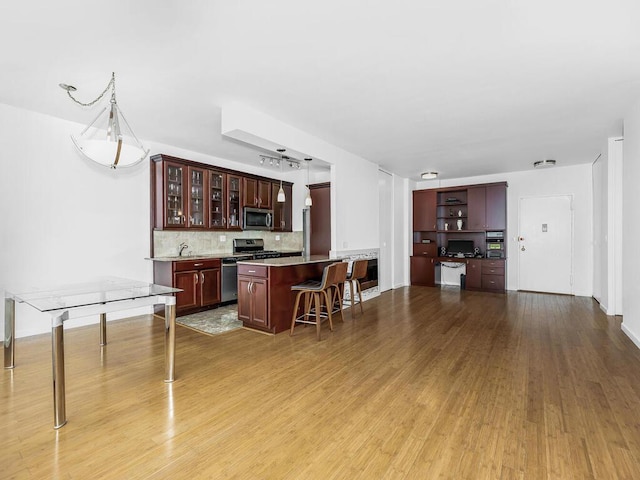 kitchen with light hardwood / wood-style flooring, decorative backsplash, a breakfast bar, a kitchen island, and appliances with stainless steel finishes