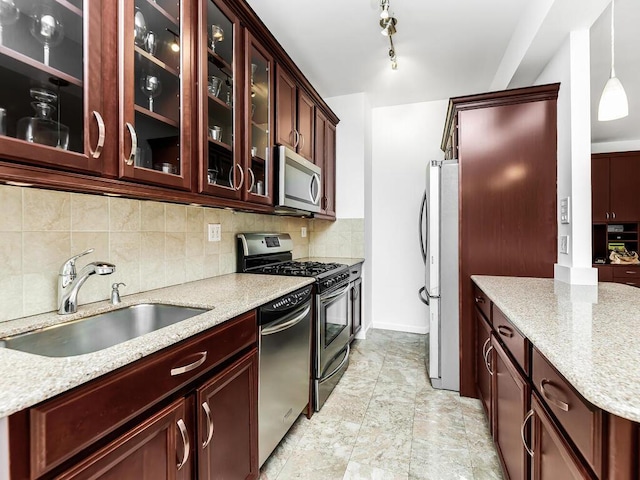 kitchen with backsplash, light stone counters, stainless steel appliances, sink, and hanging light fixtures