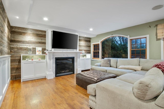 living room with wood walls, light hardwood / wood-style floors, and a high end fireplace