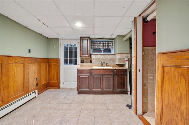 interior space with a drop ceiling, baseboard heating, sink, and light tile patterned floors