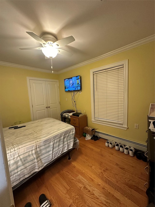 bedroom featuring ornamental molding, ceiling fan, a baseboard heating unit, hardwood / wood-style flooring, and a closet