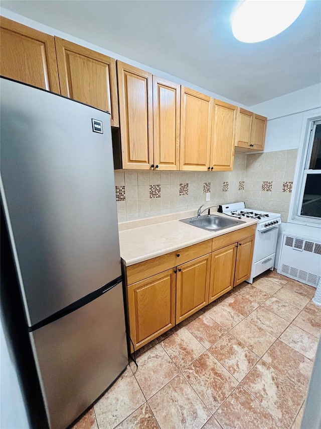 kitchen featuring stainless steel refrigerator, sink, radiator heating unit, tasteful backsplash, and white stove