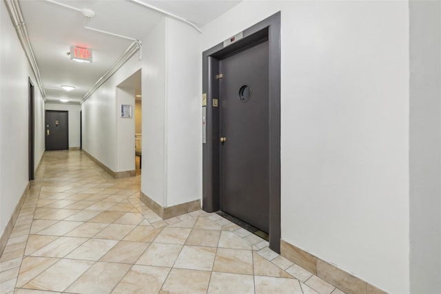 corridor featuring elevator, crown molding, and light tile patterned floors