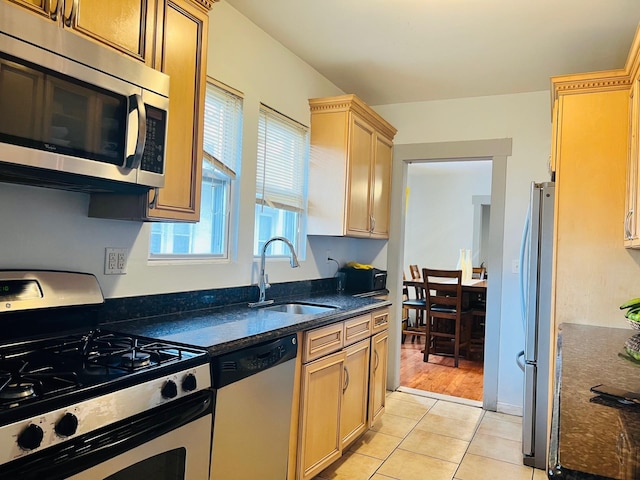 kitchen featuring light brown cabinetry, stainless steel appliances, sink, dark stone countertops, and light hardwood / wood-style floors