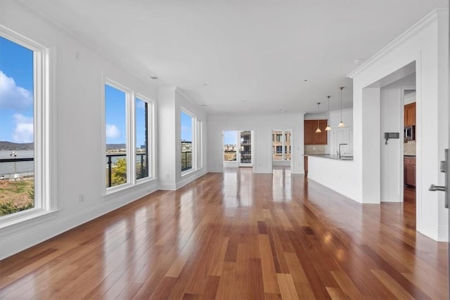 unfurnished living room featuring plenty of natural light, wood-type flooring, and crown molding