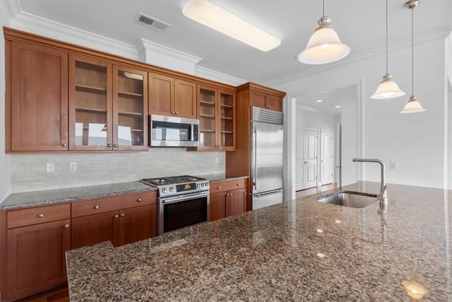 kitchen with appliances with stainless steel finishes, ornamental molding, sink, dark stone countertops, and hanging light fixtures