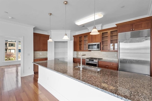 kitchen with decorative backsplash, appliances with stainless steel finishes, dark stone counters, pendant lighting, and hardwood / wood-style flooring