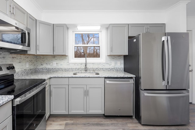 kitchen featuring sink, gray cabinets, light stone countertops, ornamental molding, and appliances with stainless steel finishes