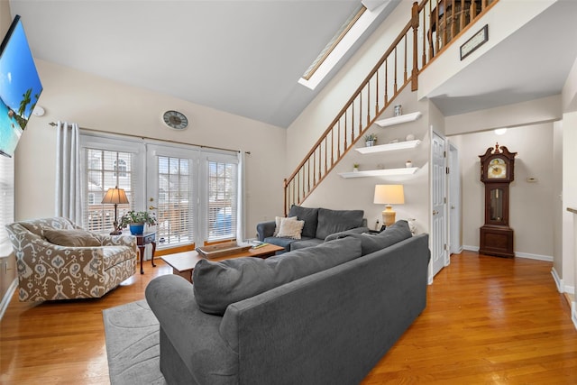 living room with high vaulted ceiling, a skylight, and light hardwood / wood-style floors