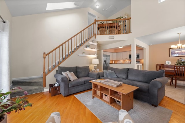 living room featuring a skylight, high vaulted ceiling, a chandelier, and light hardwood / wood-style floors