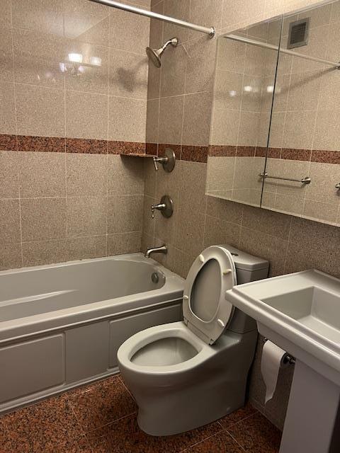 bathroom with tiled shower / bath, tile walls, and toilet