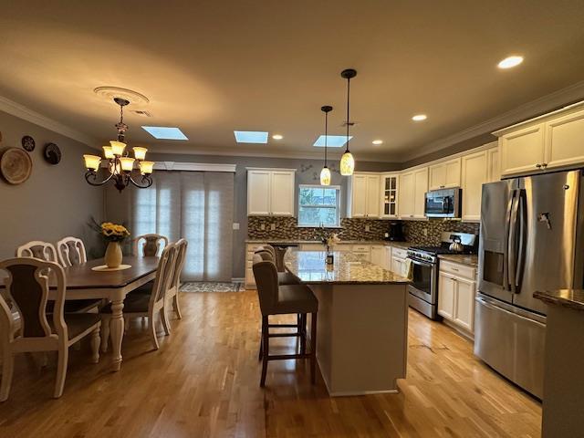 kitchen with a skylight, crown molding, pendant lighting, stone countertops, and appliances with stainless steel finishes