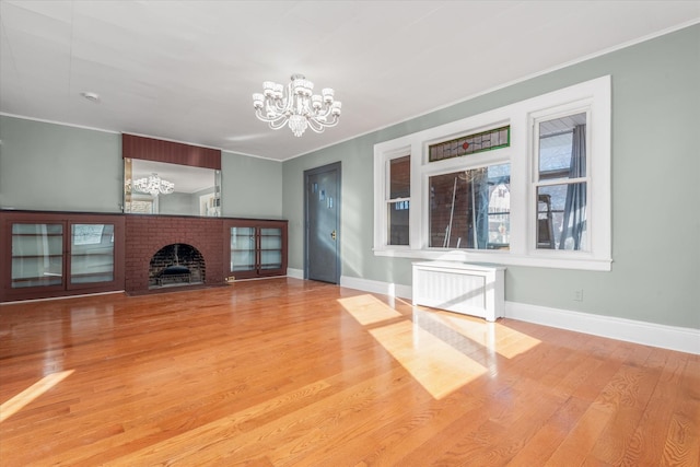 unfurnished living room featuring a brick fireplace, ornamental molding, hardwood / wood-style floors, a chandelier, and radiator heating unit