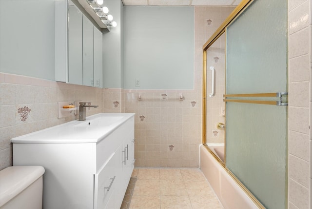 full bathroom with tile patterned flooring, combined bath / shower with glass door, toilet, vanity, and tile walls