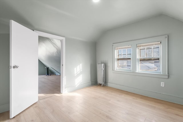 unfurnished room featuring radiator heating unit, light wood-type flooring, and lofted ceiling