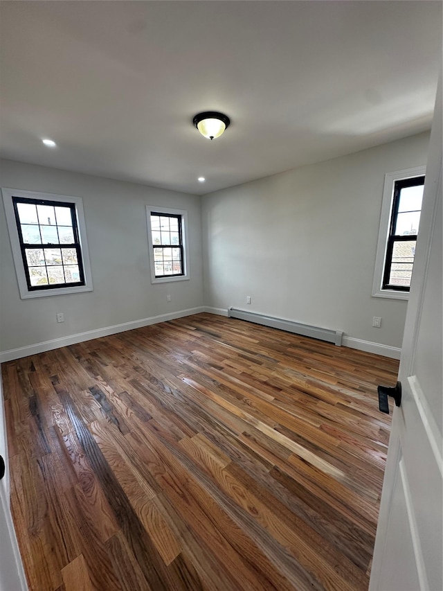 unfurnished room with a wealth of natural light, dark hardwood / wood-style floors, and baseboard heating