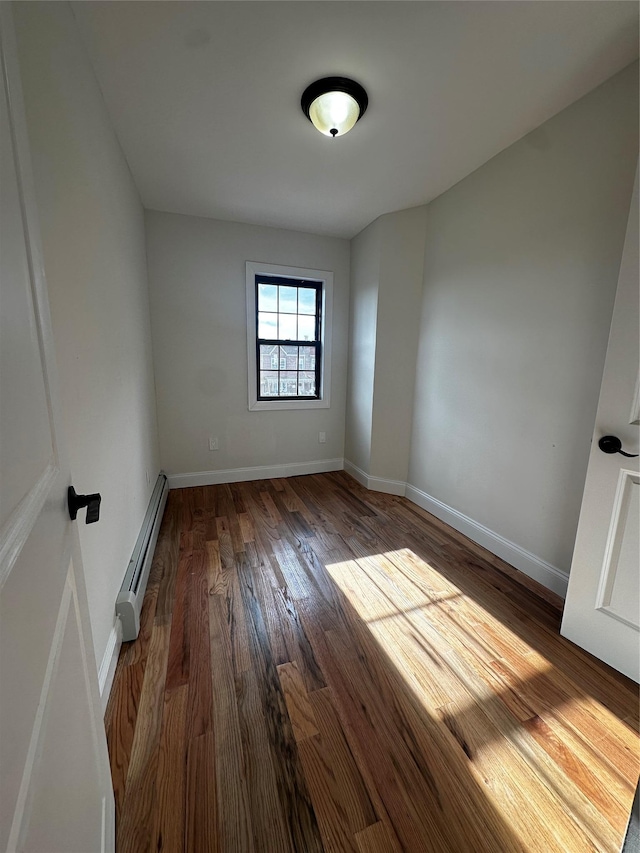 empty room with dark hardwood / wood-style flooring and a baseboard heating unit