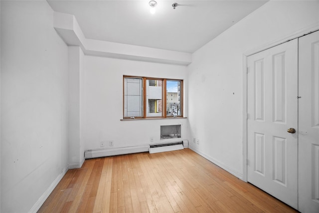 unfurnished bedroom featuring light wood finished floors, baseboard heating, and baseboards