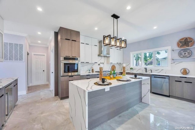 kitchen with appliances with stainless steel finishes, wall chimney range hood, white cabinets, a center island, and hanging light fixtures