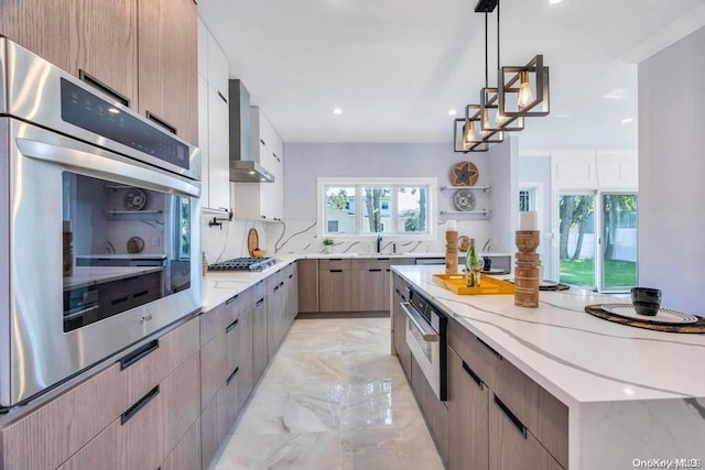 kitchen featuring sink, wall chimney exhaust hood, decorative light fixtures, light stone counters, and stainless steel appliances