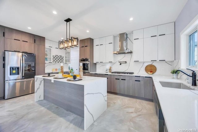 kitchen with wall chimney range hood, gas stovetop, stainless steel fridge with ice dispenser, decorative light fixtures, and a kitchen island