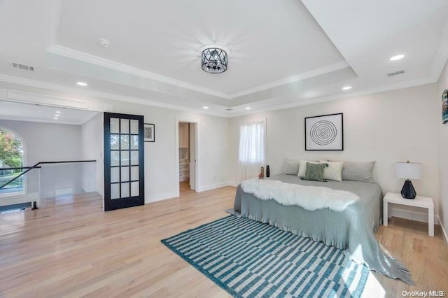 bedroom with light hardwood / wood-style floors, crown molding, and a tray ceiling