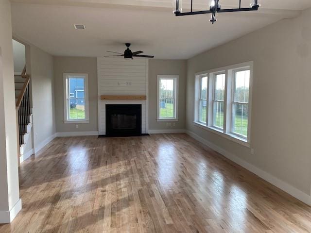 unfurnished living room featuring a large fireplace, light hardwood / wood-style flooring, and ceiling fan