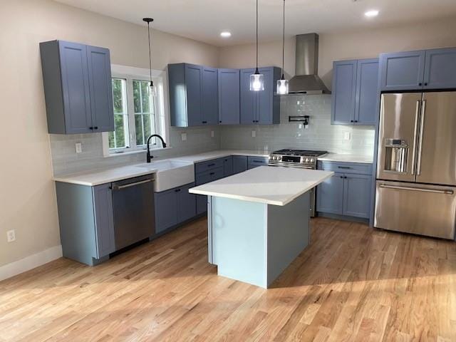 kitchen featuring appliances with stainless steel finishes, wall chimney range hood, decorative light fixtures, a center island, and light hardwood / wood-style floors