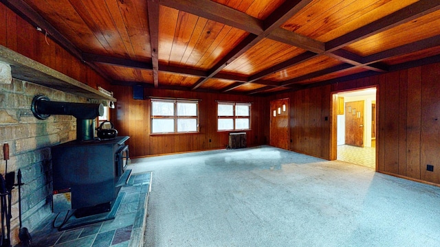 unfurnished living room with radiator heating unit, wood walls, beamed ceiling, a wood stove, and wood ceiling