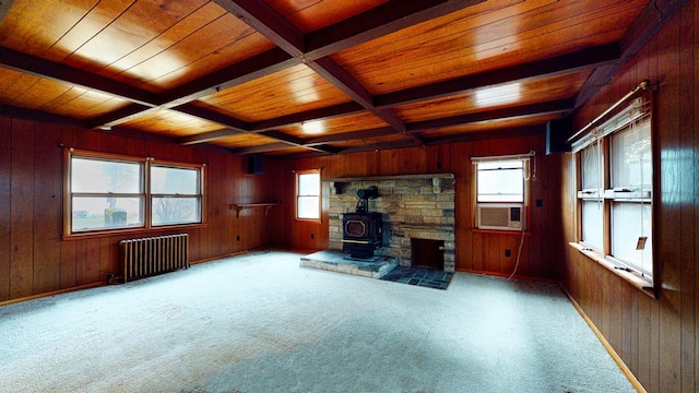 unfurnished living room with radiator heating unit, wood walls, a wood stove, wooden ceiling, and beam ceiling