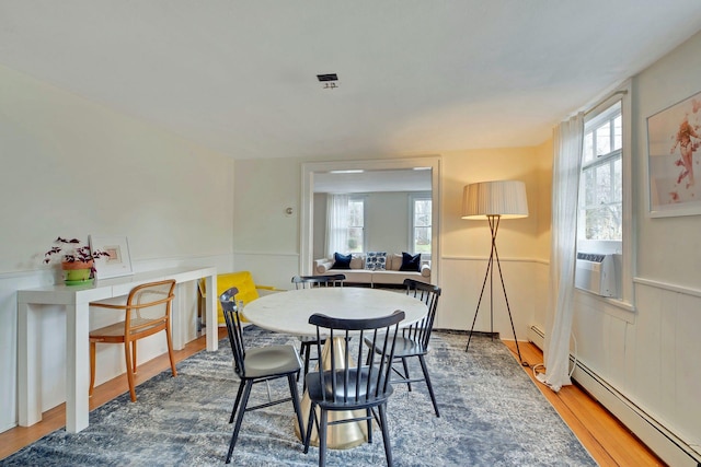 dining space featuring a wealth of natural light, baseboard heating, cooling unit, and wood finished floors