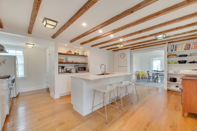 kitchen with a center island with sink, open shelves, a kitchen breakfast bar, white cabinetry, and light wood-style floors