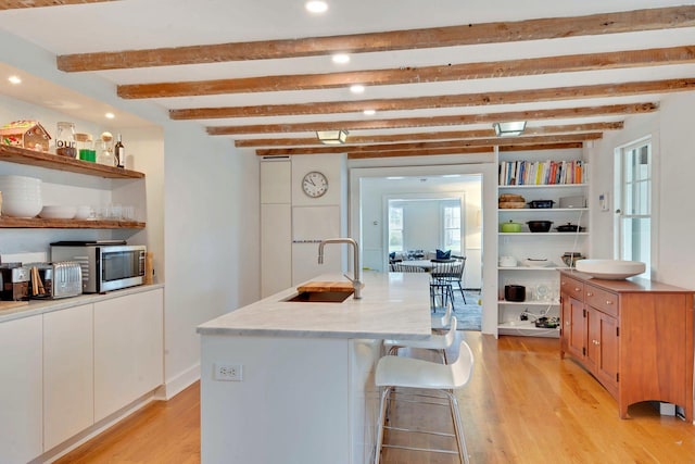 kitchen with open shelves, stainless steel microwave, light wood-style flooring, and a sink