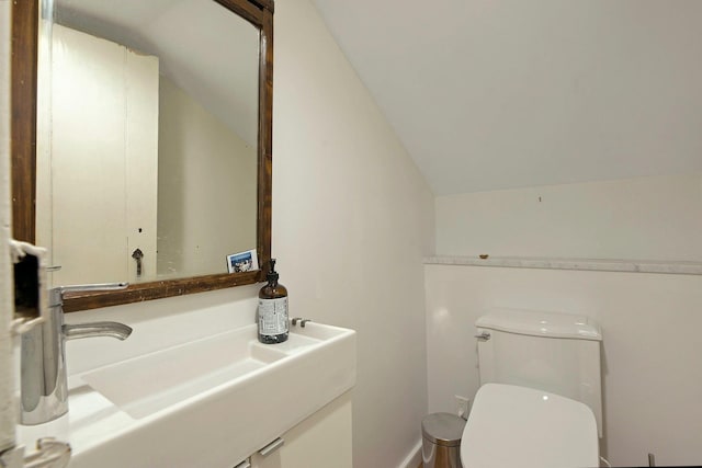 half bath with toilet, lofted ceiling, and a sink