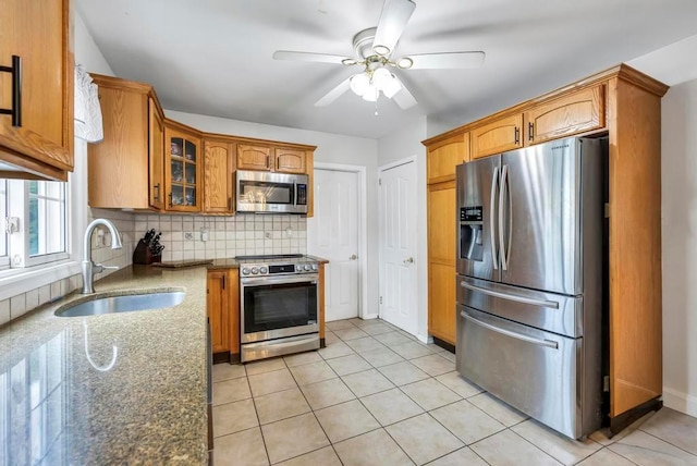 kitchen with decorative backsplash, appliances with stainless steel finishes, ceiling fan, sink, and dark stone countertops