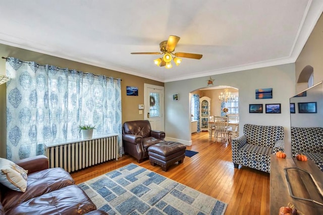 living room with ceiling fan with notable chandelier, wood-type flooring, radiator heating unit, and ornamental molding