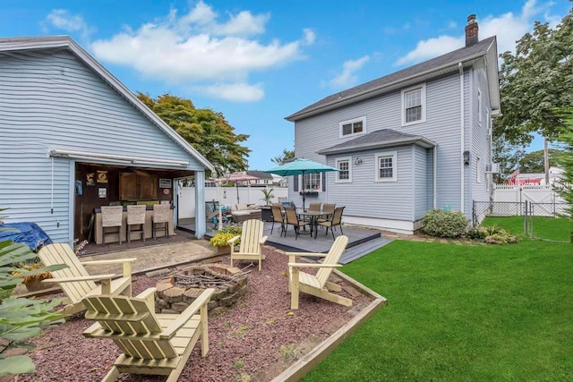 rear view of house with an outdoor bar, an outdoor fire pit, a wooden deck, and a lawn