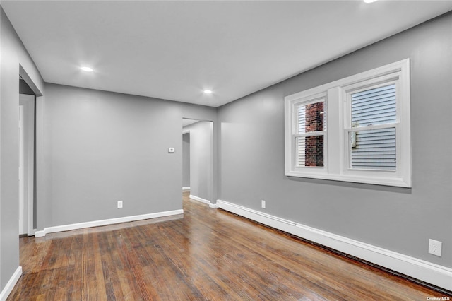 empty room with dark hardwood / wood-style flooring and a baseboard heating unit